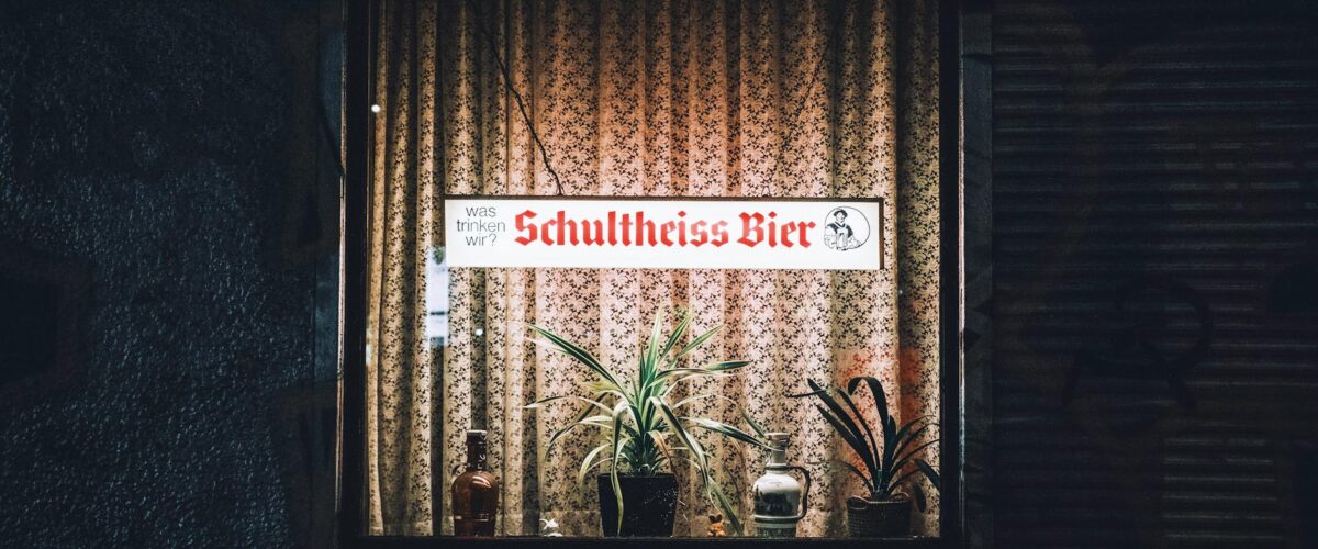 Cozy Berlin pub window display with illuminated sign and plants at night.