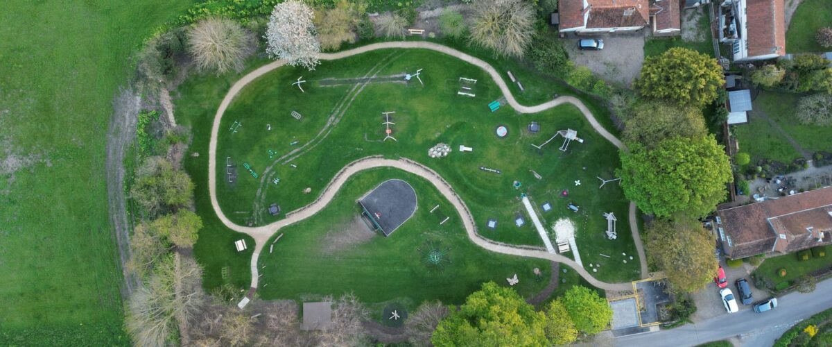 Holzspielgeräte auf einer Wiese am Dorfrand – Spielplatz Lübarser Felder in Alt-Lübars