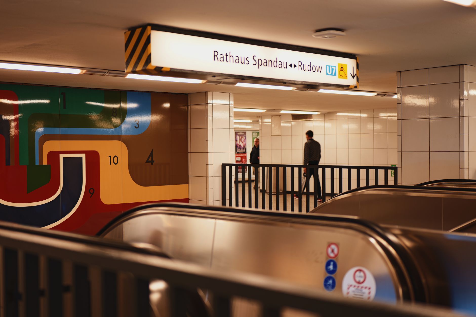 Helle, moderne Empfangshalle des Bahnhofs Spandau mit der charakteristischen gewölbten Glasdecke und Reisenden, die auf Züge warten.
