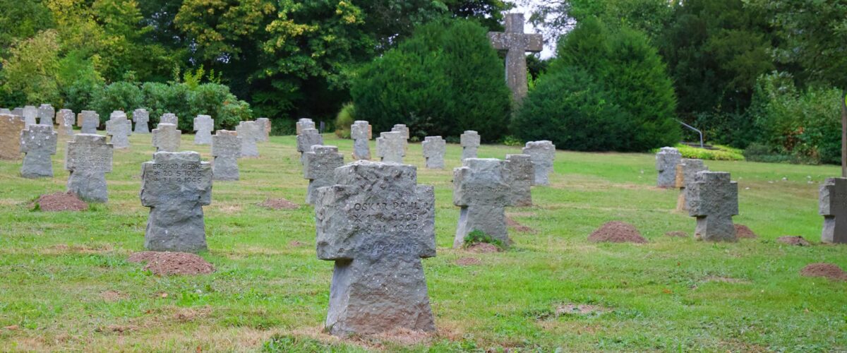 Eine von herbstlichen Bäumen gesäumte Allee auf einem Friedhof in Spandau, die an alten Grabsteinen vorbeiführt.