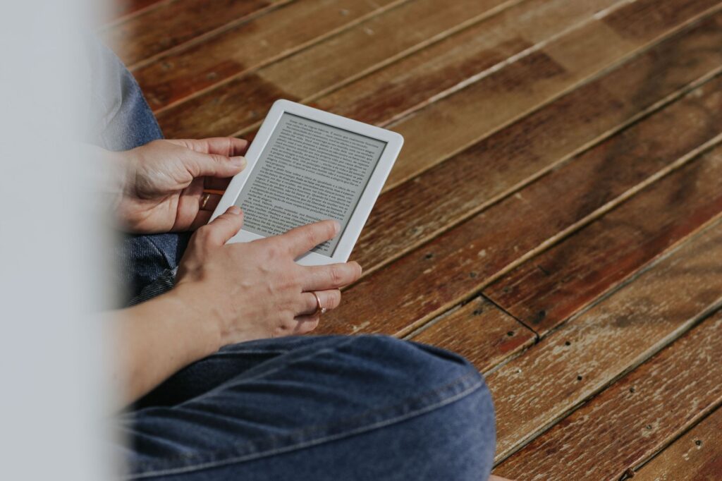 Eine Person nutzt die Onleihe der Bibliothek Reinickendorf auf einem E-Reader, im Hintergrund sind B&uuml;cherregale zu sehen.