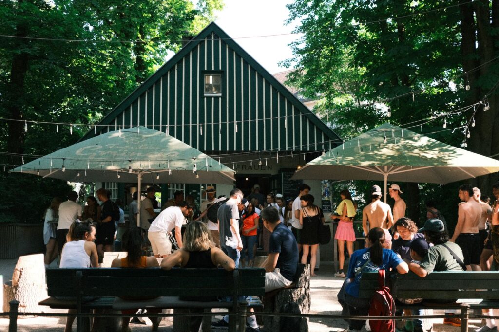 Blick auf die Terrasse eines Biergartens am Ufer des Orankesees in Berlin, mit Tischen und St&uuml;hlen.