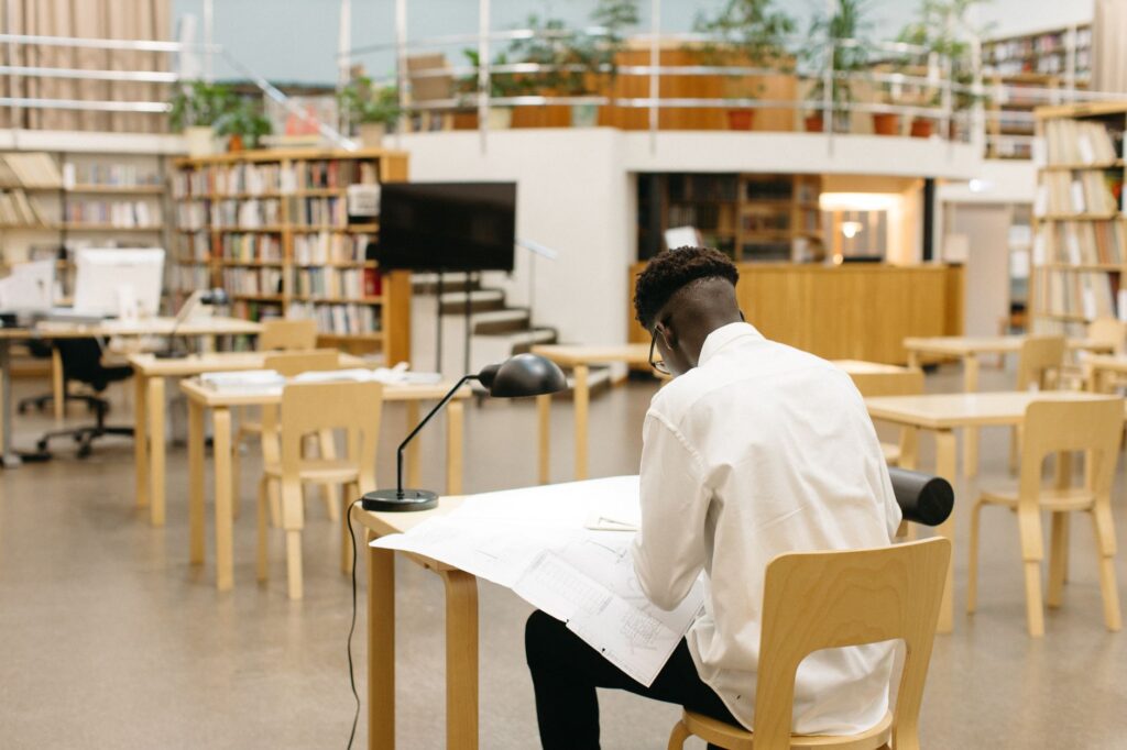 Ein Student sitzt konzentriert an einem Schreibtisch in einer Berliner Bibliothek und pr&uuml;ft Unterlagen f&uuml;r seinen WBS-Antrag.