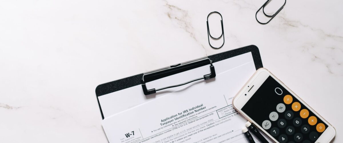 Eine ältere Person füllt am Schreibtisch einen Antrag für Wohngeld für Rentner aus, daneben liegen ein Taschenrechner und ein Mietvertrag.