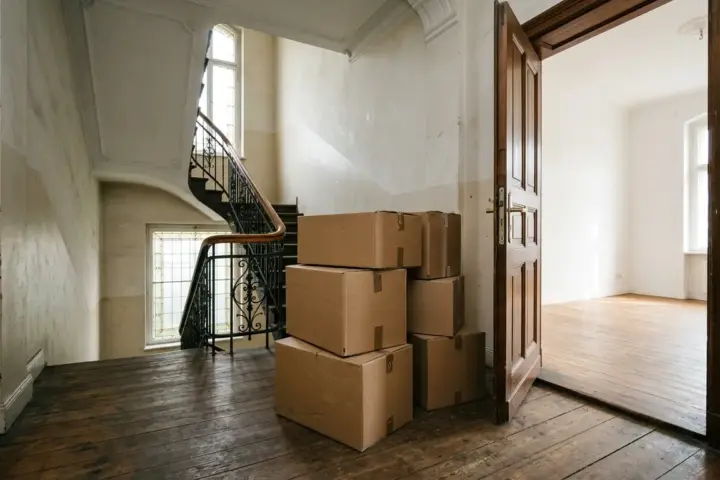 Braune Umzugskartons vor einer offenen Wohnungstür im Altbautreppenhaus beim Ummelden in Berlin.