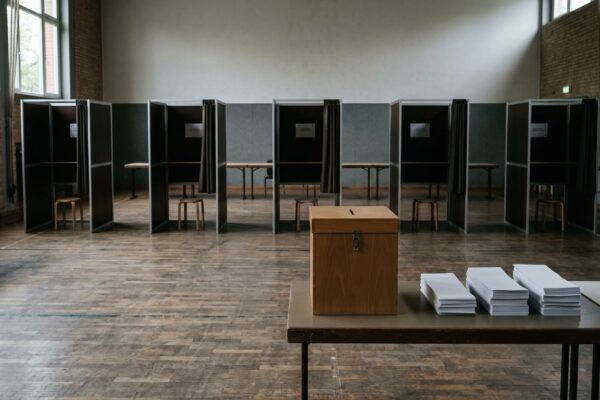 Wiederholungswahl Berlin Auszählung: leerer Wahlraum mit aufgereihten Wahlkabinen, Wahlurne und Stimmzettelstapeln, menschenleer, ohne Personen und ohne Parteilogos