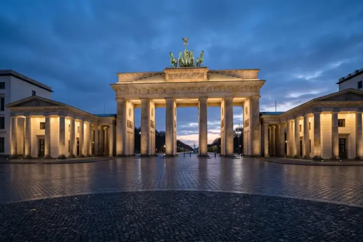Das Brandenburger Tor in Berlin bei Dämmerung, in blauem und weißem Licht angestrahlt auf leerem Platz.
