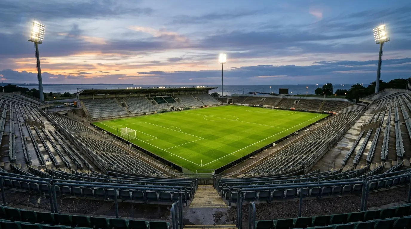 Blick in ein leeres Fußballstadion in der Dämmerung mit eingeschaltetem Flutlicht und gepflegtem grünem Rasen.