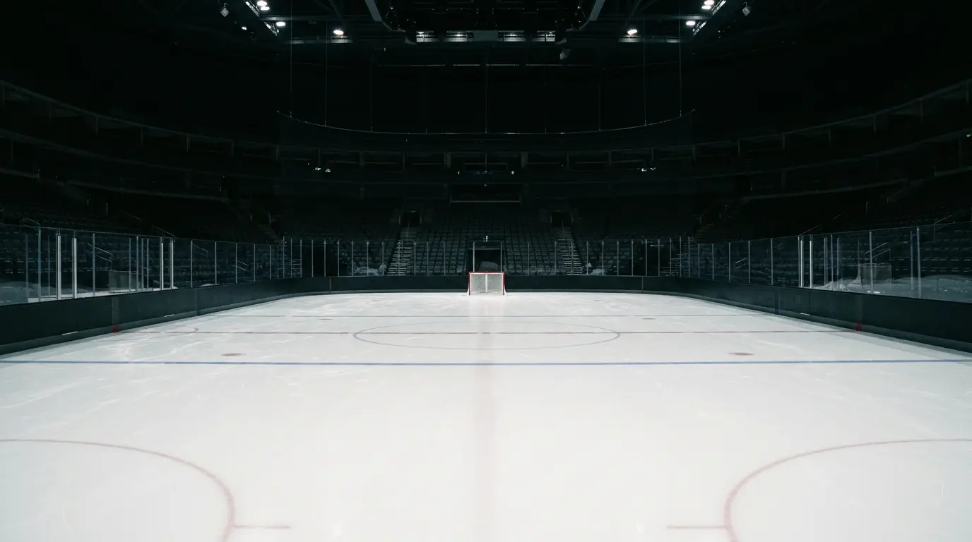 Leere Eisfläche in einer verdunkelten Eishockeyhalle mit Toren und leeren Zuschauerrängen.