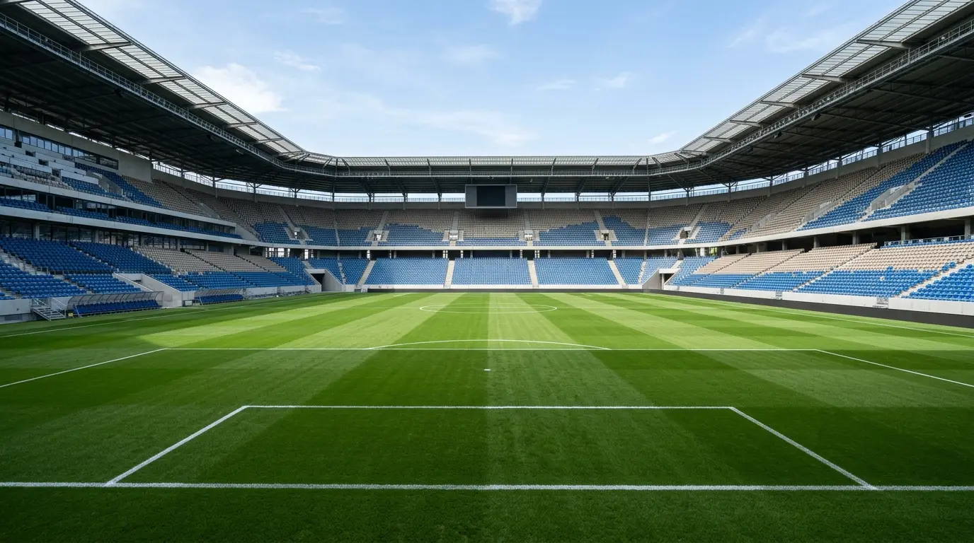 Blick über einen gepflegten grünen Rasen auf die leeren Zuschauertribünen eines großen Fußballstadions bei Tageslicht.