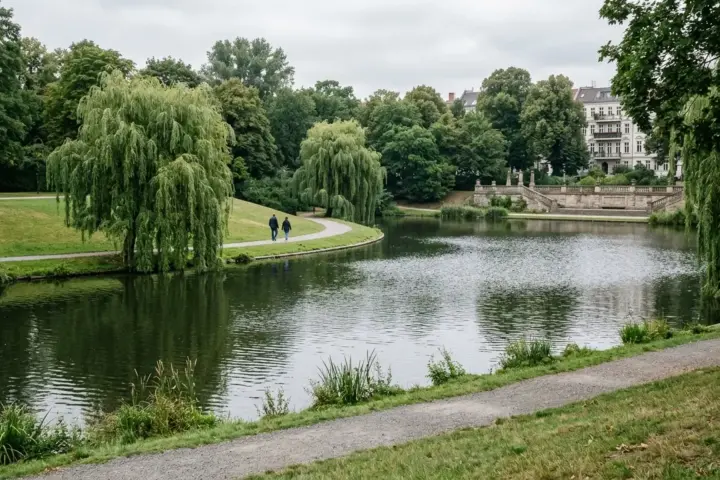 Ruhiger Lietzensee im denkmalgeschützten Park mit baumbestandenem Ufer, Grünflächen und Spazierweg an einem Nachmittag.