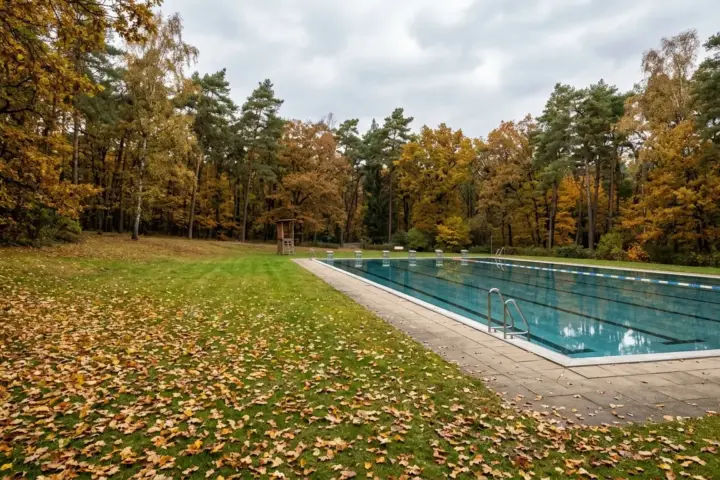 Leeres Becken im Sommerbad Wuhlheide mit stiller Wasserflaeche und herbstlichem Laub auf der Liegewiese